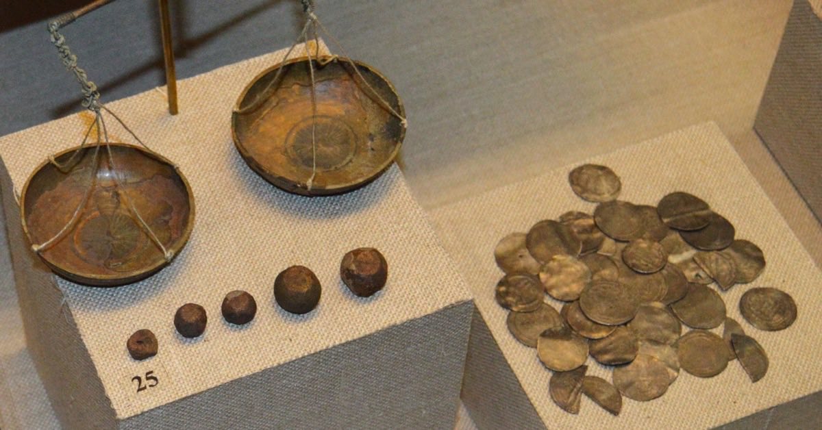 Historische Balkenwaage mit kleinen Gewichten und ein Haufen silberner Dirham-Münzen in einer Museumsvitrine